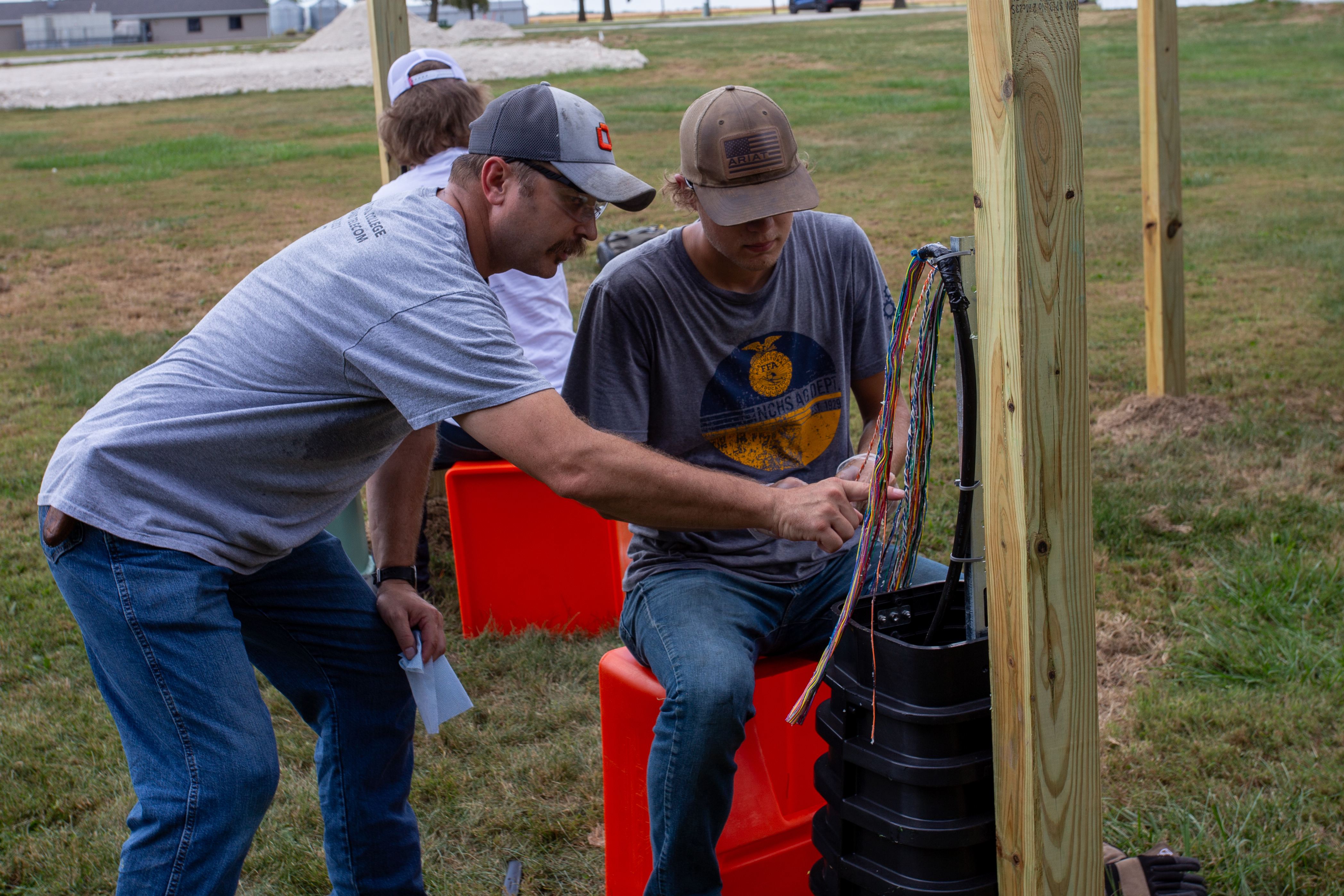 Lincoln Trail College Telecom Instructor Dennis York assisting a student with fiber optic cable installation outdoors.