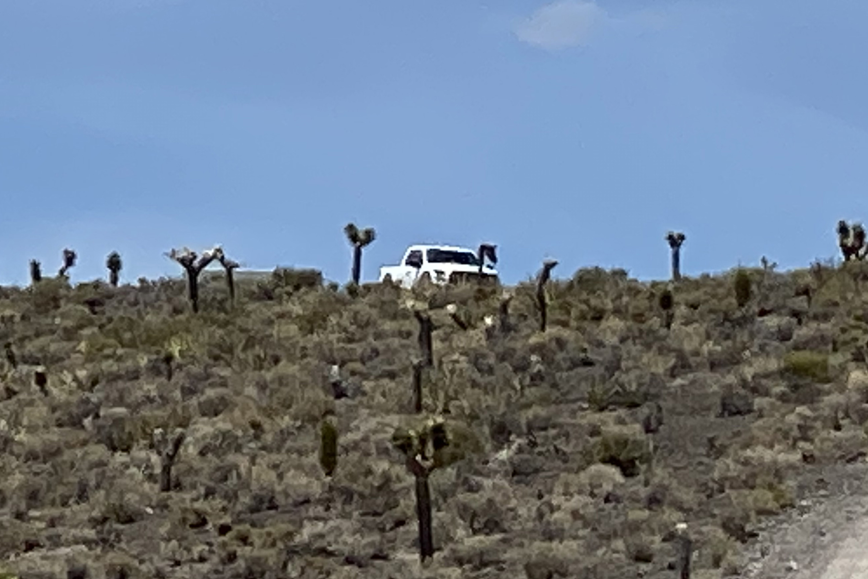 A distant white truck appears heavily pixelated and distorted due to extreme digital zoom on a phone camera. The image demonstrates how zooming in from afar can reduce clarity, introduce noise, and affect overall image quality, making details appear blurry and less defined.