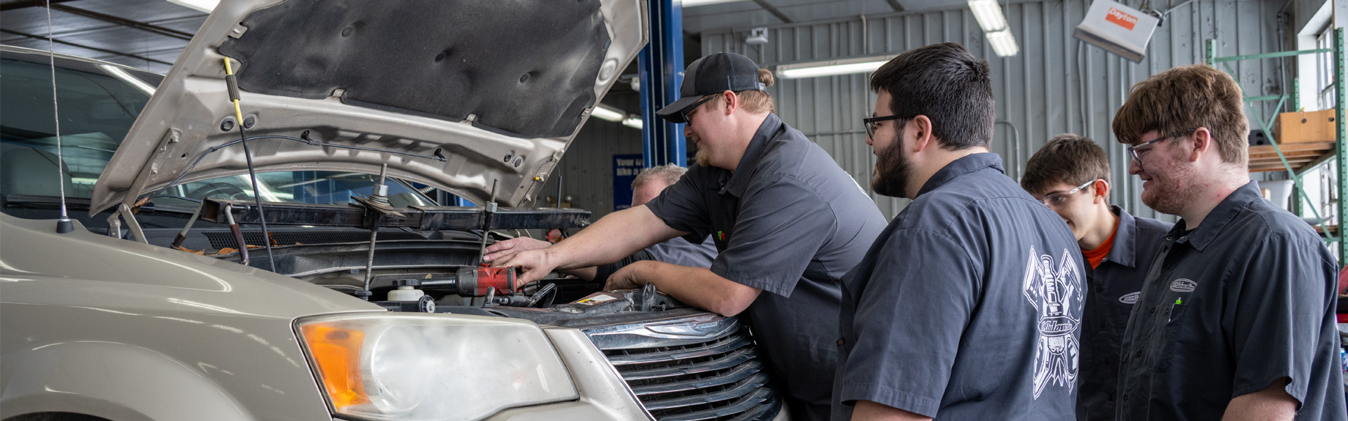 Student is working on car engine with three other students watching