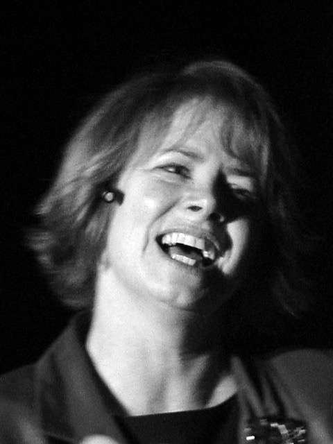 Barbara Shimer smiles while performing on stage under dramatic lighting during a musical or theater production.