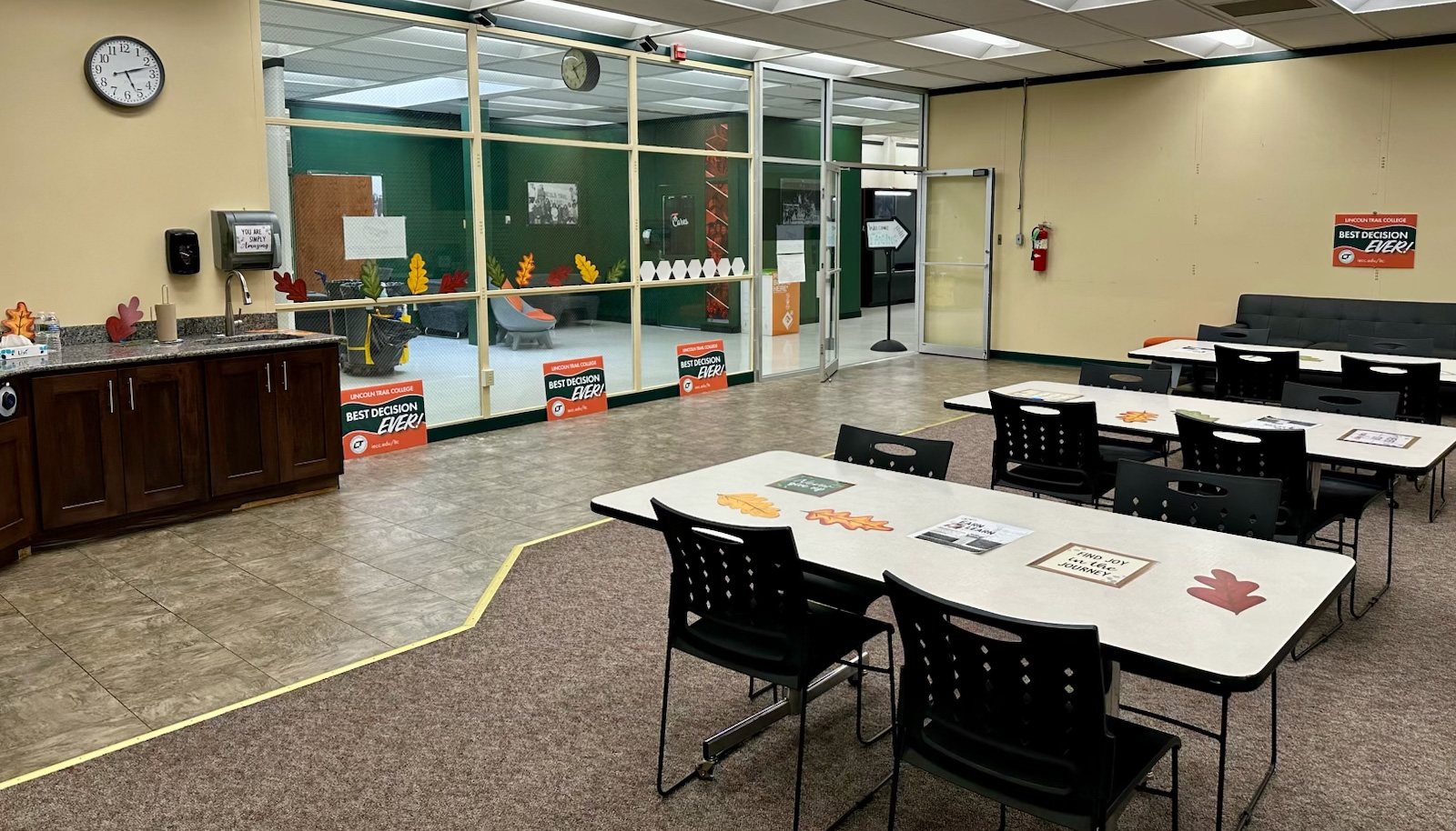 The Landing at Lincoln Trail College features tables and chairs for studying and gathering, a kitchenette, and a glass-walled adjoining lounge. The space is decorated with autumn leaves and Best Decision Ever campaign signs.