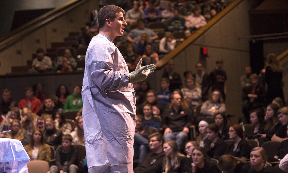 Board certified orthopaedic surgeon Dr. Julko Fullop commentates on the total knee replacement happening behind him on stage. Photo courtesy of TJ Hug of The Prairie Post.