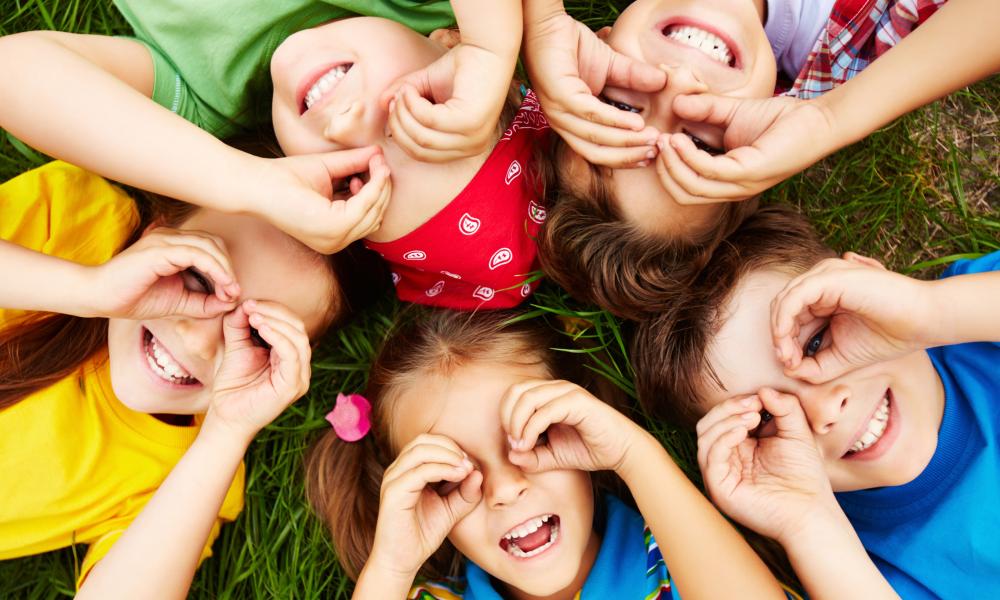 Group of children laying on ground using their hands like binoculars