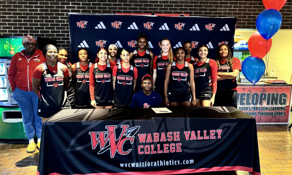 B Waheed Signs with St. John's University with support of the Lady Warriors Basketball Team behind her