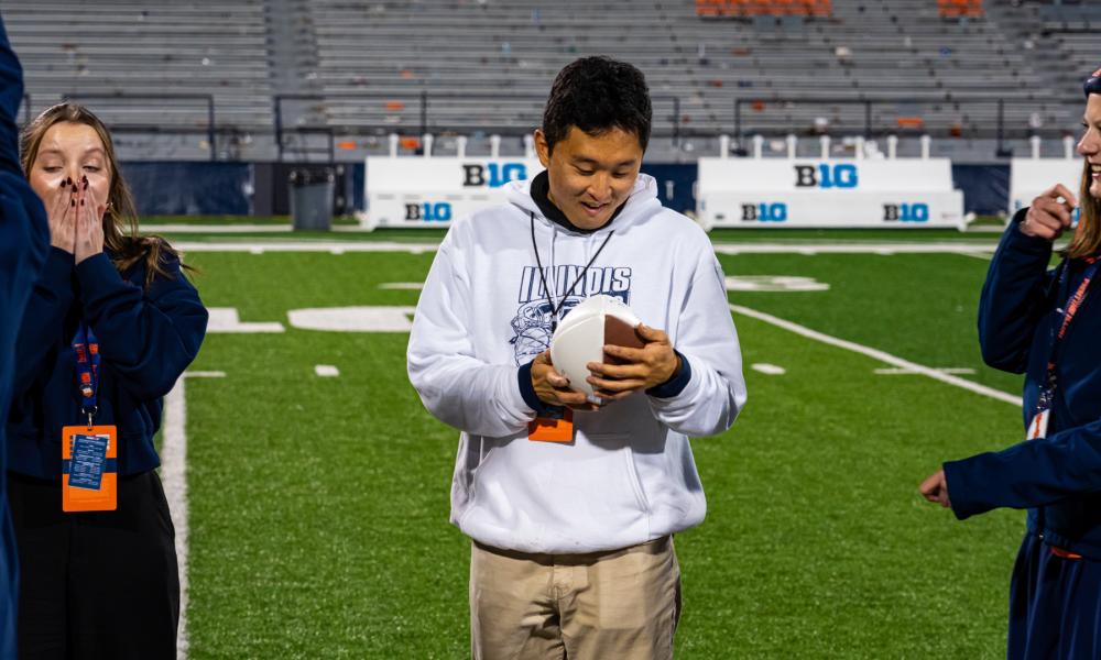 A photo of Cy Yun holding a football where he looks surprised and happy