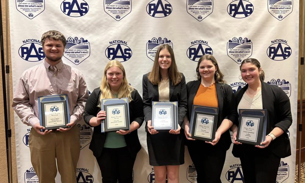 Five WVC students standing in front of a National PAS step‑and‑repeat backdrop at a conference, each holding a framed award plaque and wearing business attire.