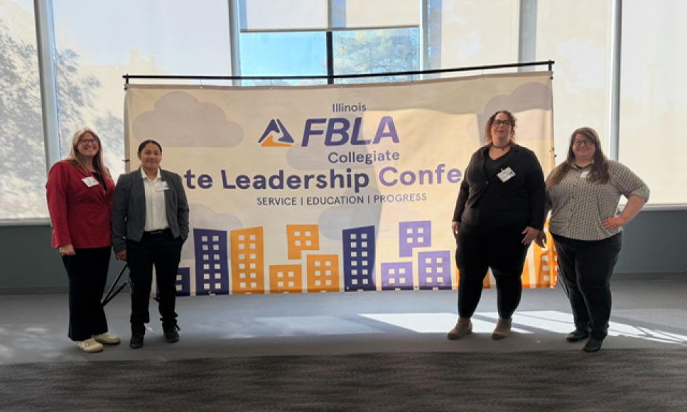 Amie Mayhall, Emelyn Rivera, Jessica Wagner, and Brandy Cochran pose in front of an Illinois FBLA Collegiate State Leadership Conference banner, standing in a bright indoor space with large windows and a cityscape graphic backdrop.