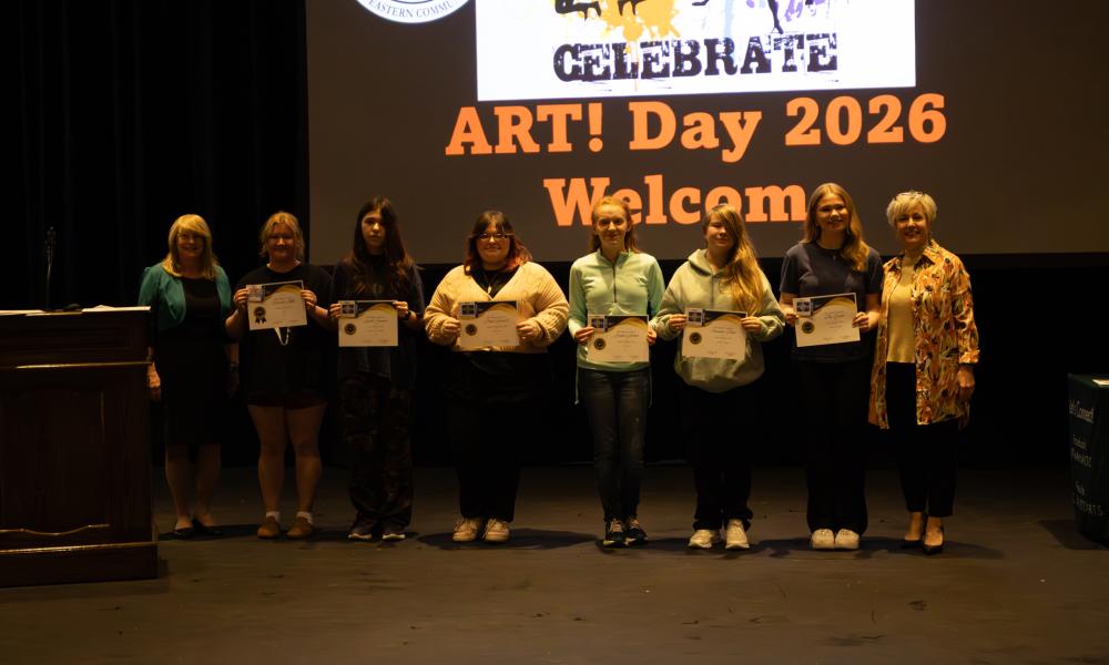 Celebrate Art! award winners stand on stage holding certificates during the 2026 event, posing with organizers in front of a large “Celebrate Art! Day 2026” screen.