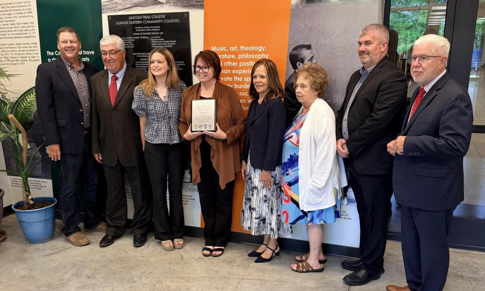 Illinois Eastern Community Colleges Trustee Barbara Shimer poses with fellow Board of Trustees members and family members while holding a plaque during her final board meeting at Lincoln Trail College.