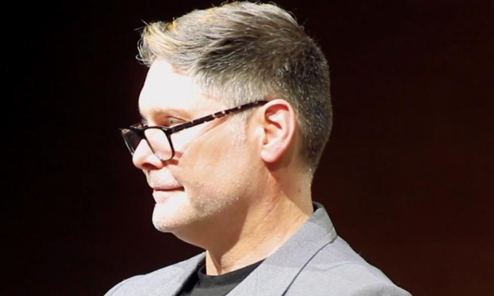 A profile view of Dr. Stewart Cramer. He is looking to the left wearing black glasses and a grey suit.