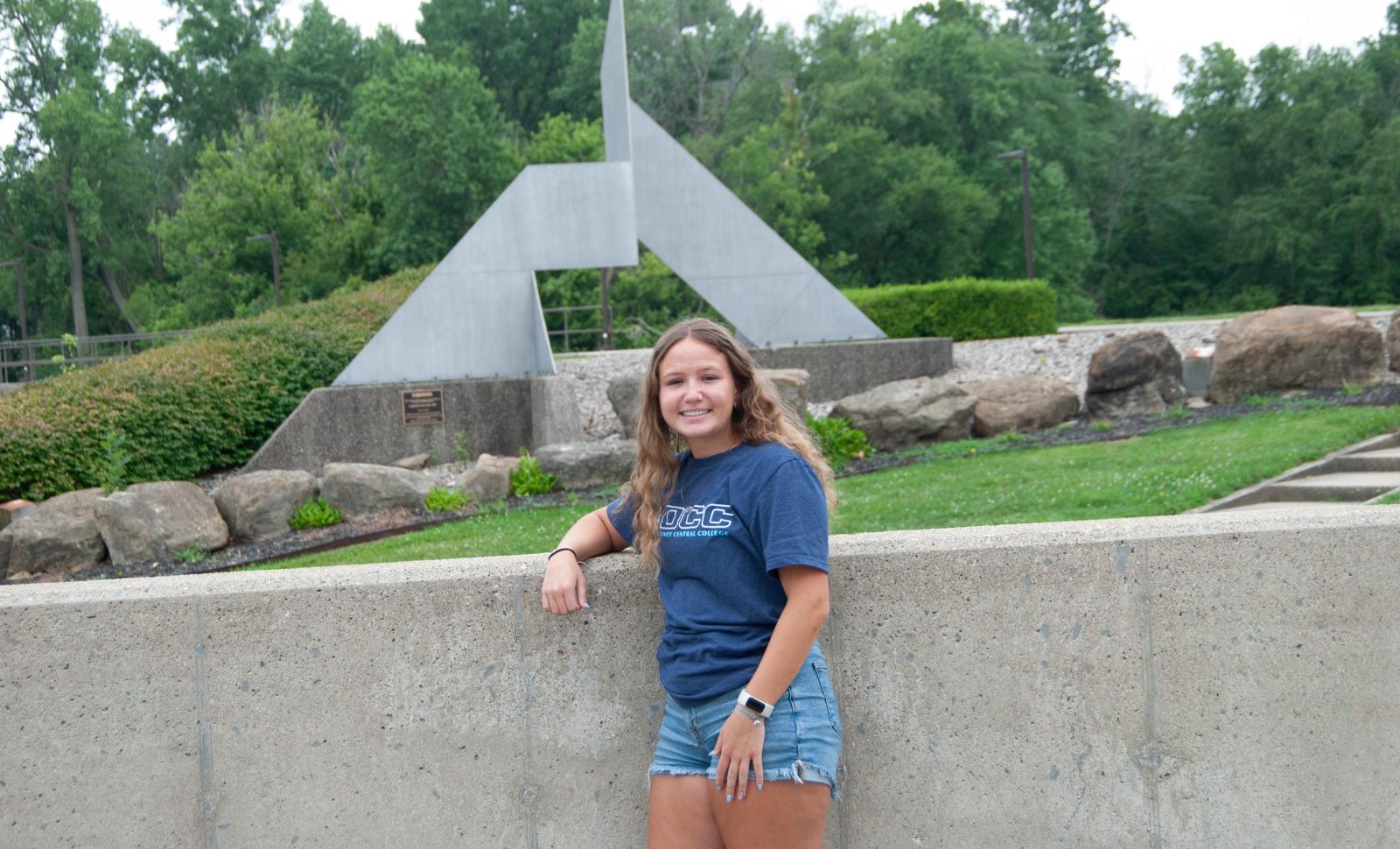 A friendly Olney Central College student standing in front of a sculpture smiling
