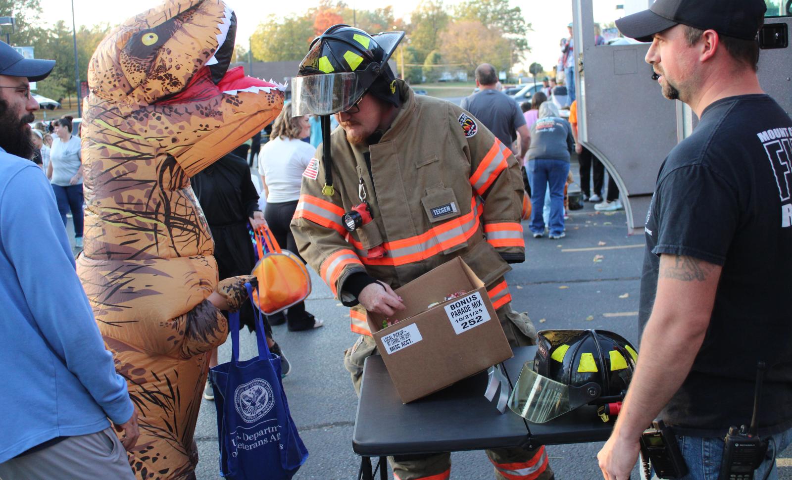 Fireman looks in trick or treat bag of kid dress as a T-Rex