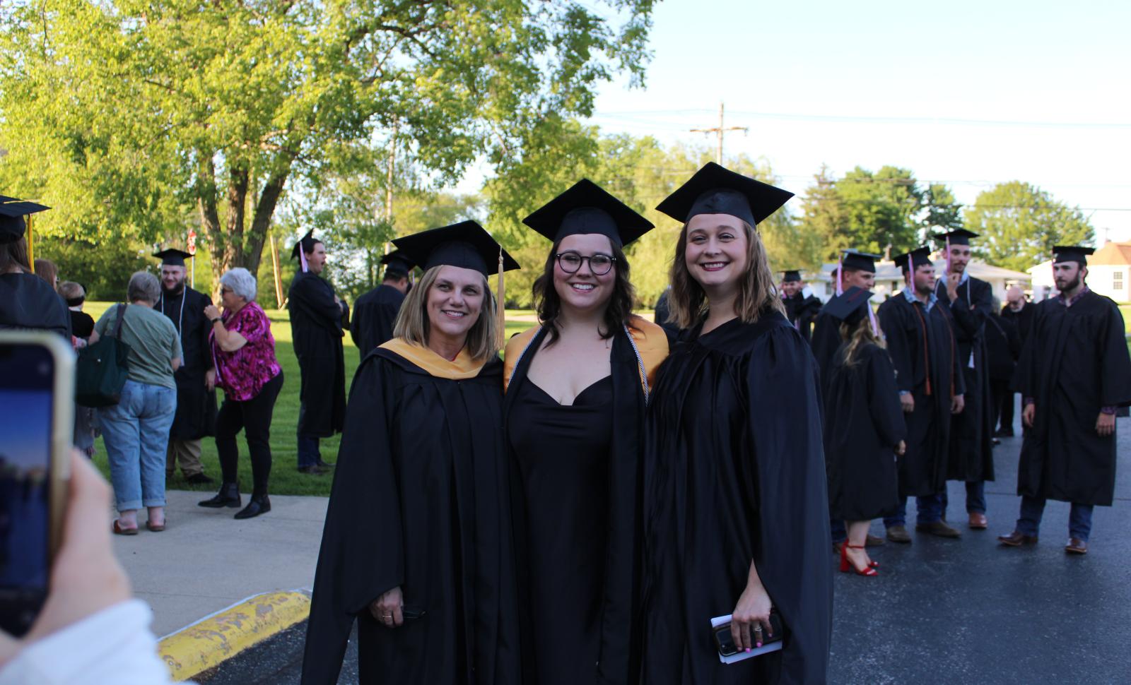 Three individuals in cap and gown posing for a photo outside of the WVC sports center