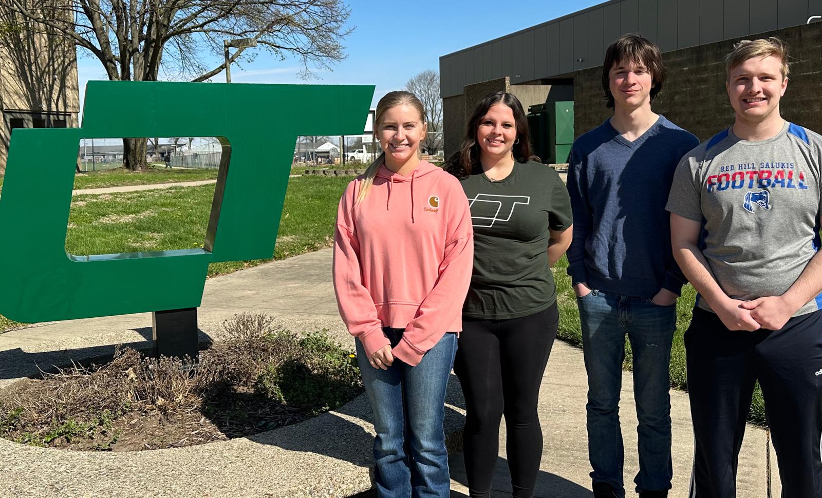 Four Lincoln Trail College students—Hannah Potts, Natalie Ramsey, Korbin Alger, and Dalton Spahn—stand outdoors near a large green LTC logo on a sunny day, smiling for a group photo.