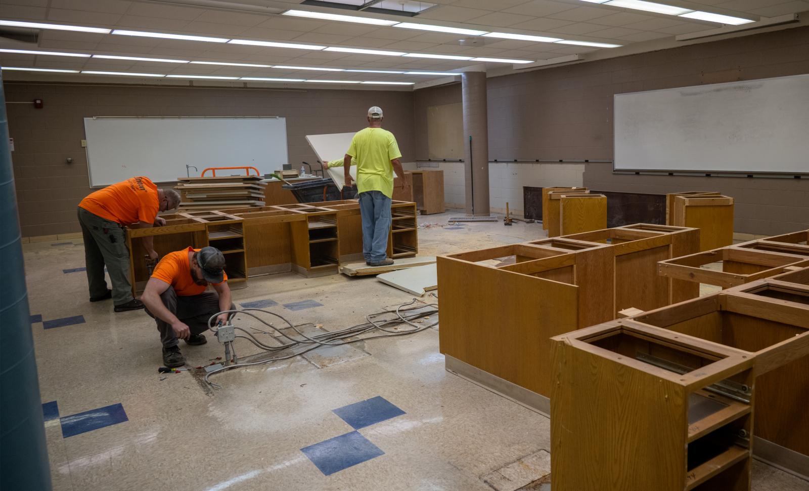 Three workers remove furnishings from a science lab