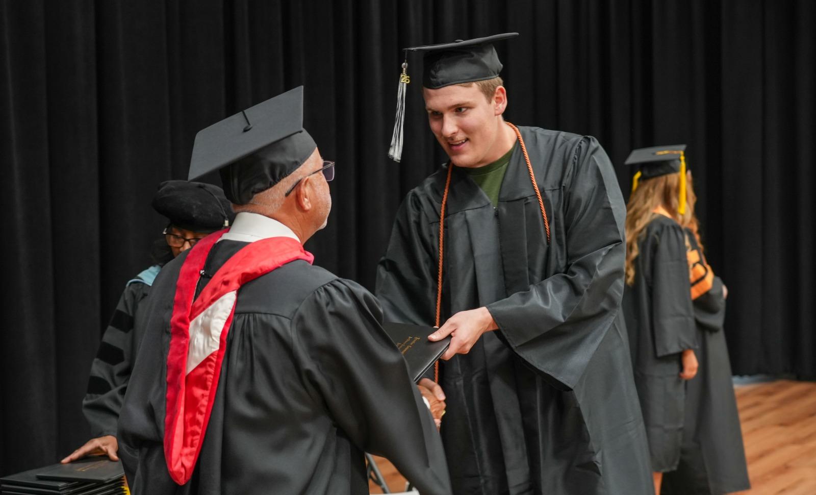 A graduate candidate walks across the stage to receive his diploma.