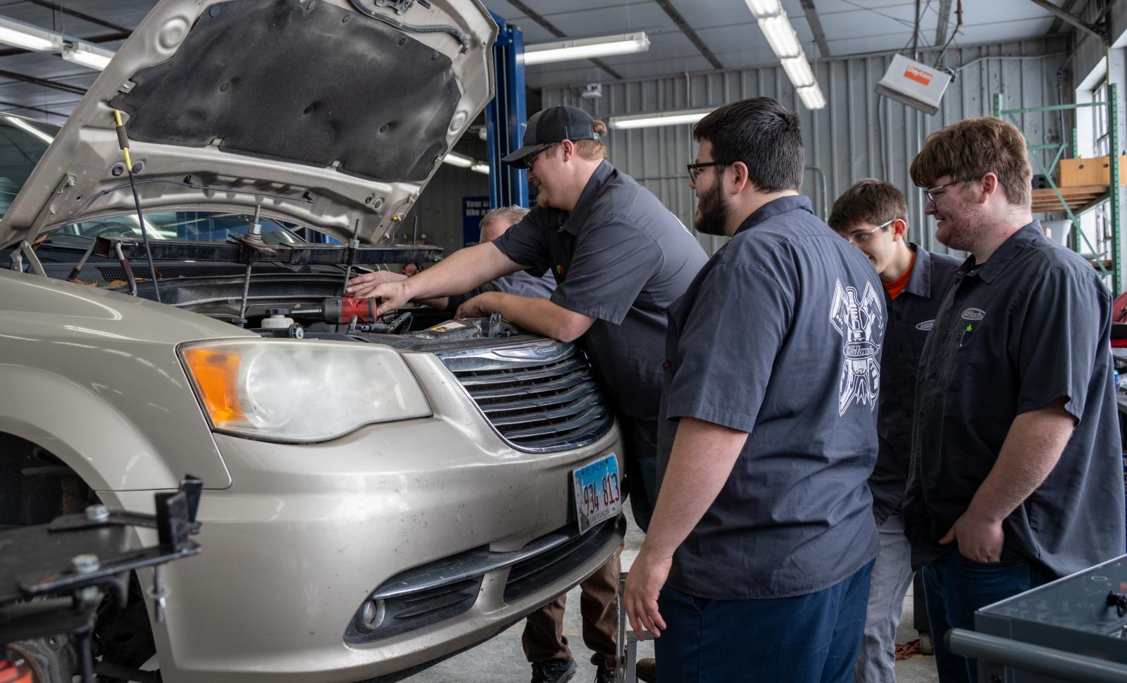 Students surround a car and work on the engine.