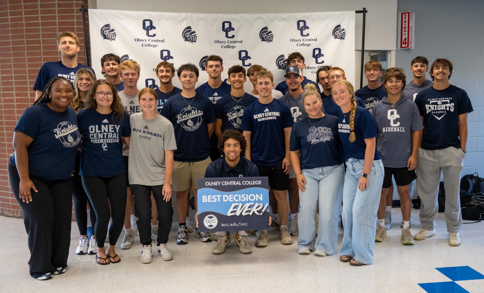 Large group of students wearing OCC shirts with the student in the middle holding a Best Decision Ever Sign