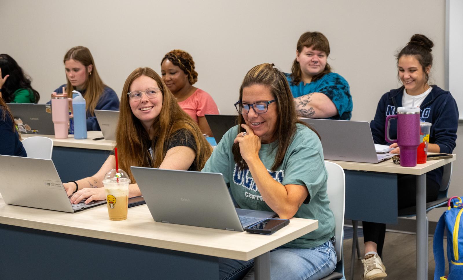 Students smiling and looking at lab tops while sitting in the classroom.