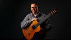 A portrait of Ben Gateno seated holding an acoustic guitar