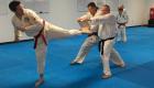 A Taekwondo student kicks and breaks a board held by two martial arts instructors