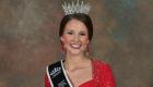 Lincoln Trail College alumna Krista Phillips smiles in a formal portrait wearing a jeweled crown and sash after being named State Fair Queen. She is dressed in a red gown with matching earrings, posed against a neutral studio backdrop.
