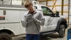 A Lincoln Trail College Broadband Telecom student stands in a workshop wearing safety glasses and protective gloves while carefully stripping insulation from a cable. He works in front of a white utility truck labeled “Lincoln Trail College Broadband Telecom,” with tools and equipment visible in the training space behind him.