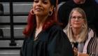 WVC Student wearing black graduation cap and gown smiling while audience members in the back admire graduate