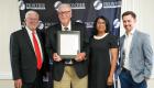 IECC Board Chairman Gary Carter, Jerry Cox holding a framed proclamation in his honor, FCC President Dr. Sharmila Kakac, and FCC Foundation President Luke Harl stand together in front of a Frontier Community College backdrop.