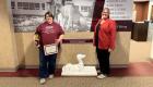 Jessica Wagner (left) holds a certificate and award while standing beside Amie Mayhall (right). They pose in a campus hallway, celebrating Wagner’s accomplishments at the SIU Accounting Competition, with a dog statue and display signage behind them.