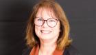 Alt text: Portrait of Illinois Eastern Community Colleges Trustee Barbara Shimer smiling in front of a dark background. She is wearing glasses and a black jacket with brown lapels.