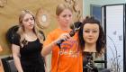 A camper uses the curling iron on a manikin with a cosmetology student watching