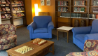 Image of 4 cozy lounge chairs in the corner of a space in the Learning Commons. Tall bookshelves along the walls and coffee table has board games on it.