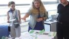 Jessica McDonald shares the story of a Holocaust survivor with two individuals standing on either side of her. She is pointing to related documents on a table.