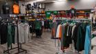 Interior of the Statesmen Store at Lincoln Trail College, featuring racks and wall displays of college-branded shirts, sweatshirts and athletic apparel in green, orange, black and gray, with fall decorations throughout the store.